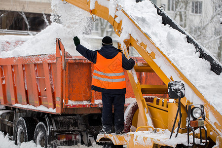 爪式装载机车辆清除道路上的积雪 穿制服的社区服务人员帮助将雪装进卡车背景