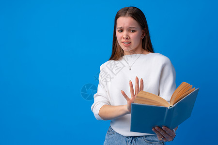 年轻美女拿着书本 惊吓和惊讶 在工作室的蓝背景看着高清图片素材