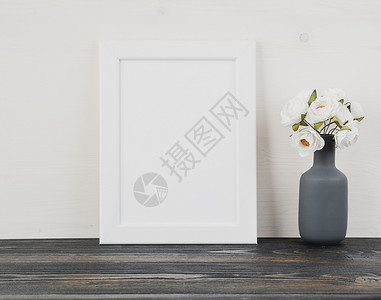 木框架样机白框 花瓶里的花 深灰色木桌上的时钟 靠着白墙 有复制空间背景