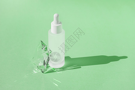 绿色魔法状光效白瓶中含有胶原蛋白和肽的血清护肤产品 绿色背景上带有滴管 带有水晶玻璃棱镜折射光效和光线 产品样机包装背景