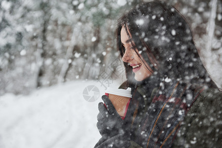 在树林中下雪 女孩穿着温暖衣服 喝着咖啡的女孩在冬天的森林里散步树木高清图片素材