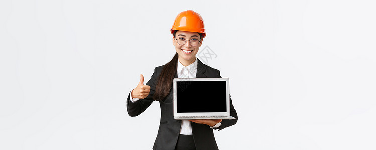 微笑的专业女建筑师 工厂的施工经理显示图表 正图 竖起大拇指表示认可并手持笔记本电脑屏幕 戴安全头盔女孩领导者投资者建设者企业家背景图片