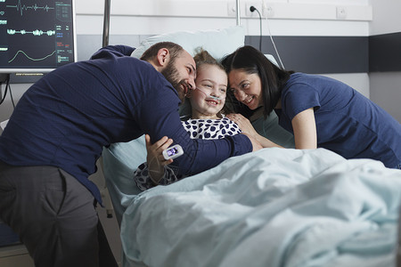 在儿科医院病房里 快乐的年轻父母拥抱生病住院康复的小女孩女儿高清图片素材