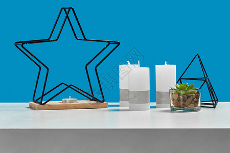 石头烛台白色桌子上有绿色多汁植物 三支大蜡烛和一支小烛台 呈铁星 黑色三角形的形式 蓝色背景 特写背景
