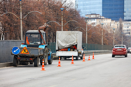 市政公用一队道路服务人员驾驶着一辆旧的公用拖拉机和一辆卡车 正在用橙色锥体围住一段道路 以便进行后续清洁背景