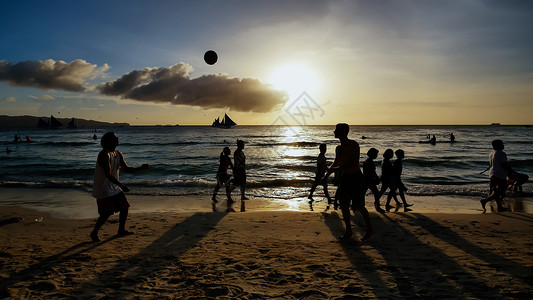 中球节在傍晚日落的光芒中长滩岛的海滩 在沙滩上玩球的人和在水面上航行的帆船的剪影地平线家庭阳光运动假期血管风光射线风景冲浪背景