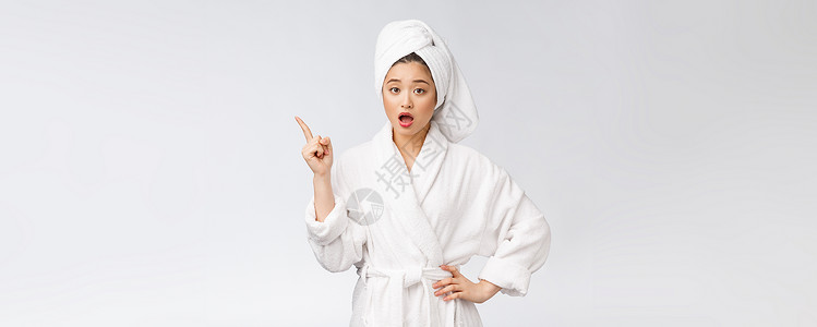年轻女性的美容肖像显示并指向空空间复制 浴袍中的亚洲美护理治疗展示成人女士微笑女孩广告身体皮肤背景图片