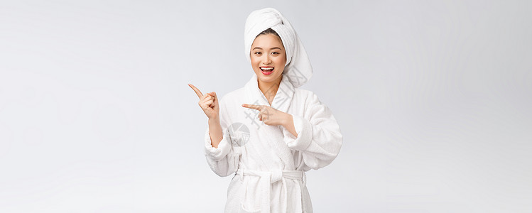 年轻女性的美容肖像显示并指向空空间复制 浴袍中的亚洲美护理女孩皮肤快乐广告展示化妆品手指女士成人背景图片
