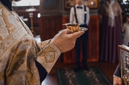 一位身穿金色大衣的牧师 拿着一小杯圣红酒祝福高清图片素材