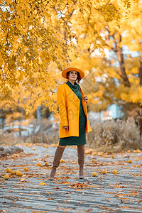美丽的女人在秋天到户外散步 她身穿黄色外套 黄色帽子和绿色连衣裙 享受秋天天气的少妇 秋季内容叶子女士冒充毛衣围巾季节微笑头发快落下高清图片素材