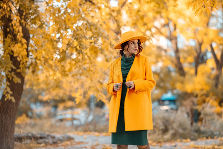 美丽的女人在秋天到户外散步 她身穿黄色外套 黄色帽子和绿色连衣裙 享受秋天天气的少妇 秋季内容微笑季节冒充落叶公园头发毛衣女士晴生活方式高清图片素材