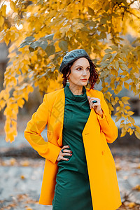 美丽的女人在秋天到户外散步 她穿着一件黄色外套和一条绿色连衣裙 享受秋天天气的少妇 秋天的内容日落乐趣帽子冒充皮肤青年微笑毛衣快女性高清图片素材