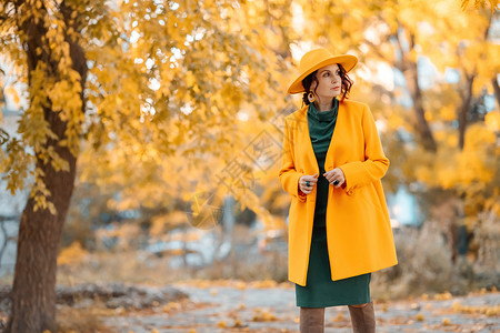 美丽的女人在秋天到户外散步 她身穿黄色外套 黄色帽子和绿色连衣裙 享受秋天天气的少妇 秋季内容青年树叶微笑落叶幸福皮肤公园毛衣季头发高清图片素材