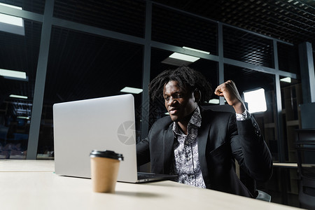 带着紧握拳头的快乐黑人正在看笔记本电脑屏幕 并高兴地完成了他的工作爆炸商务思考成人经理微笑管理人员工人人士职场背景