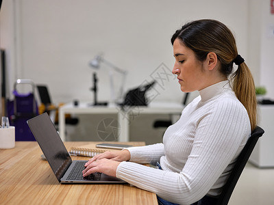 一位在桌面上与计算机一起工作的有进取心的妇女的侧面视图背景图片