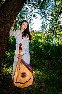 身着白裙子的乌克兰妇女站在河边一棵树下 乌克兰音乐家与一位全国连带乐队传统高清图片素材