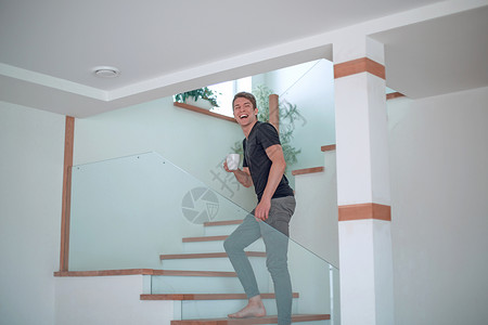 带着智能手机的笑着人站在他家的楼梯上互动装潢家庭装修住房房间技术微笑男性衣服背景图片
