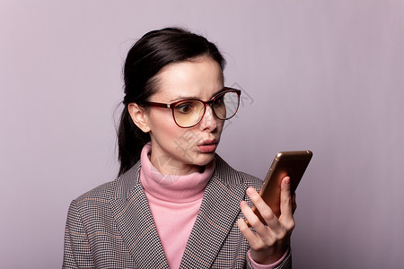 穿粉红色高领衣 灰色夹克 眼镜眼镜的女人 在灰色背景的电话上进行交流办公室工人黑发手机工作室商业学生互联网商务白色连接高清图片素材