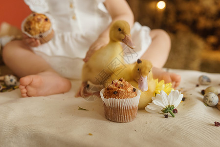 带小旗子蛋糕复活节桌上可爱的毛茸茸的小鸭子 旁边是一个小女孩 上面放着鹌鹑蛋和复活节纸杯蛋糕 复活节快乐的概念幸福婴儿传统房间桌子裙子小姑娘背景