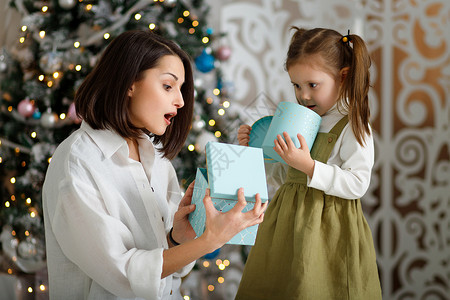 开年盛典可爱的小女孩和她妈妈 在舒适的客厅里 在圣诞树旁边 开一个神奇的圣诞礼物背景