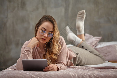 戴眼镜的金发女性 穿便衣 躺在床上 用手戳头 用平板电脑工作 学生 博客设备高清图片素材