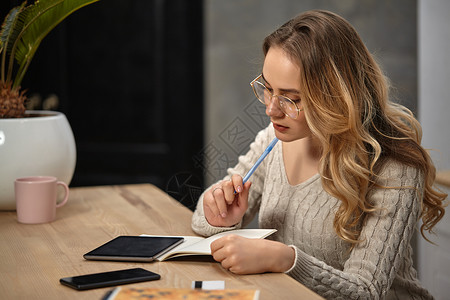 戴眼镜的模范 米色毛衣 坐在桌子上 用杯子和手掌放在桌上;在笔记本中写一些东西社会的高清图片素材