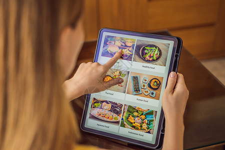 年轻妇女用平板电脑订餐 在线午餐店铺菜单技术购物手指屏幕食物互联网桌子笔记本背景图片