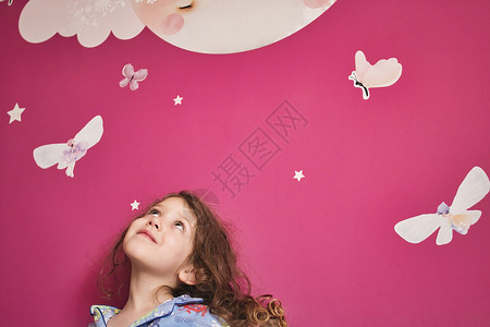 接露珠女孩穿着睡衣的年轻可爱女孩 仰望着粉红色的墙壁 上面有露珠星星 月亮和仙女背景