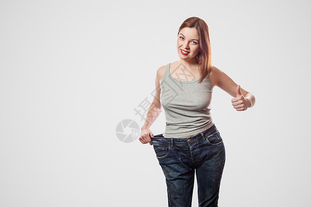穿着大牛仔裤和灰色最上衣的年轻女子 快乐而美丽的瘦瘦腰肖像 显示体重成功减肥背景图片