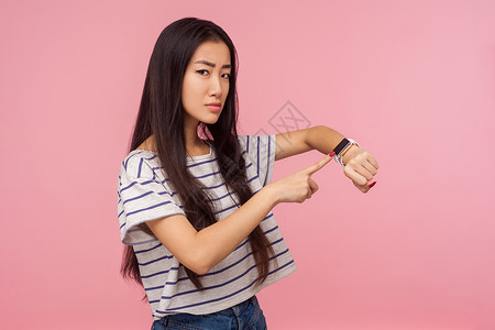 粉红色背景的亚洲年轻女性肖像老板手表检查小时手腕条纹女士长发t恤手指不高兴高清图片素材