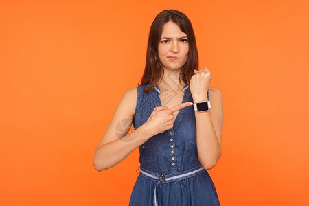 以橙色背景为背景的年轻情感女性的肖像老板女孩手势女士警告检查焦虑手腕手表黑发紧张的高清图片素材