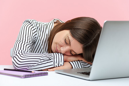 疲劳的女办公室工作人员睡觉时用笔记本电脑靠着头坐在桌子上午睡高清图片素材