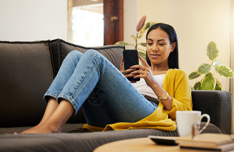 哈沙克西班牙裔女性在明亮的客厅里舒适放松地使用智能手机 一名年轻女性躺在沙发上 在家中使用现代技术在家里用手机发短信背景