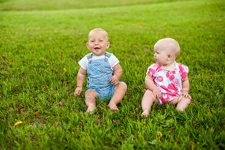 小对月草两个快乐的男婴和一个9个月大的女婴 坐在草地上交流 聊天 互相看对方背景