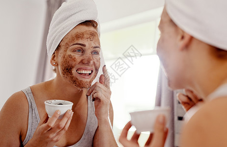 我对这个新例程感到非常兴奋 一位迷人的年轻女子站在家里浴室的镜子前 脸上敷着咖啡面膜背景图片