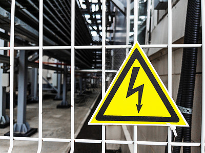 黄色金属三角形危险信号 在金属网格上的黄色三角形的高压电压电气安全冒险注意力风险栅栏技术变压器力量闪电背景