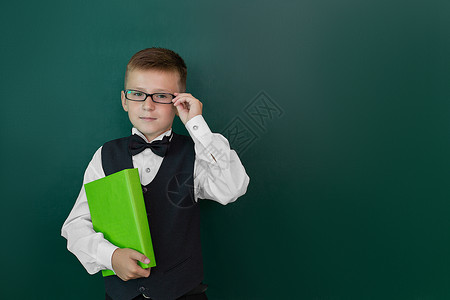 带着领结和眼镜的可爱聪明男孩手握着一本书 第一次上学 回到学校里去孩子女性手指乐趣男生喜悦瞳孔教育黑板幼儿园孤立高清图片素材
