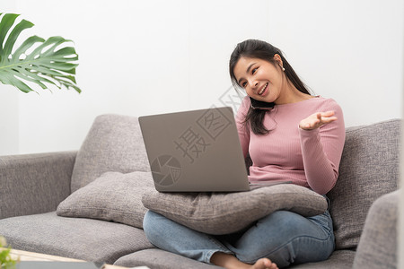 在家沙发上用手机和笔记本电脑打来电话的年轻快乐女性生活方式高清图片素材