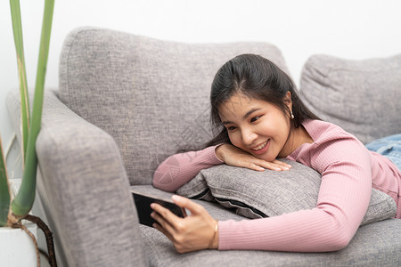 在家沙发上使用手机的年轻快乐女性社会的高清图片素材