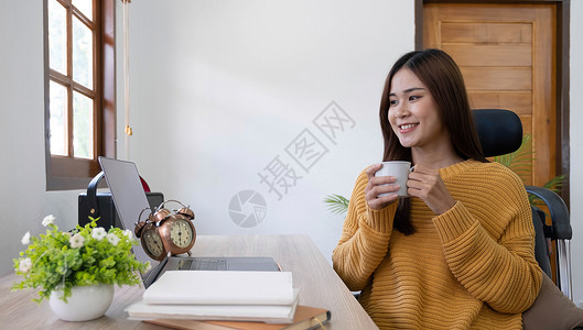 饮料杯里女孩智能中国女孩Ceo专家坐在桌边工作 远程笔记本电脑文字打字报告的侧面相片 在室内装着饮料杯教育微笑技术企业家杯子停留女孩会议咖啡背景