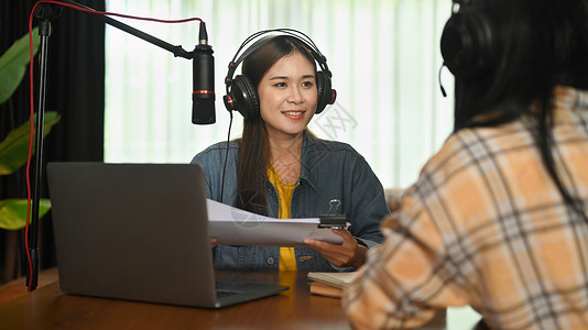 在家中演播室的电台访谈访客谈话中 带着耳机微笑的无线电主持人和录音声音桌子高清图片素材