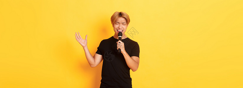 英俊的男性歌手 韩国人唱着歌 在卡拉OK用麦克风 用激情和热情地在黄色背景上站立潮人工作室理发职业发型学生广告促销购物头发肖像高清图片素材