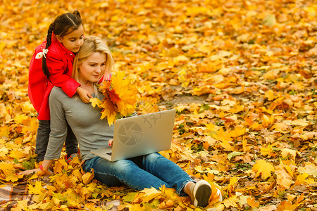 秋天简单女孩都市妇女和女儿在公园里带着笔记本电脑 穿着牛仔裤的苗条时髦女人使用笔记本 使用通信技术远程工作和环保生活方式的自由职业者大学自由背景