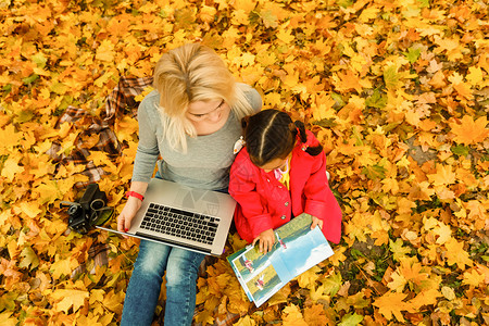 秋天简单女孩都市妇女和女儿在公园里带着笔记本电脑 穿着牛仔裤的苗条时髦女人使用笔记本 使用通信技术远程工作和环保生活方式的自由职业者女性互联背景