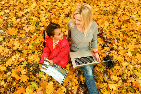 秋天简单女孩都市妇女和女儿在公园里带着笔记本电脑 穿着牛仔裤的苗条时髦女人使用笔记本 使用通信技术远程工作和环保生活方式的自由职业者博主自行背景