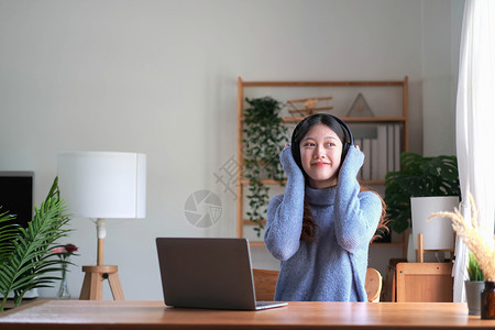 快乐的亚洲女人坐在家里的椅子上听电脑上的音乐 早上带着耳机放松的微笑女孩休息复制空间女性电话歌曲课程长椅女士列表播放青少年幸福应用高清图片素材