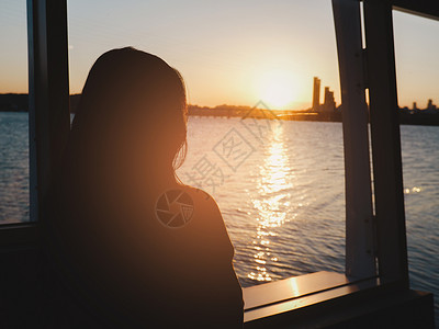 女孩和船孤单的女人看着日落 夜里海和城市的景色背景