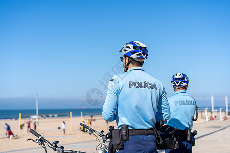 两名警察骑着自行车巡逻海边列车 人们在大西洋海岸的城市公共海滩晒太阳 美国海军陆战队警官旅游头盔安全天空街道长廊民众海洋热带背景图片