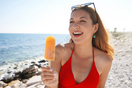 棒棒糖女孩可爱的年轻姑娘夏天在海滩吃橘子冰棒背景