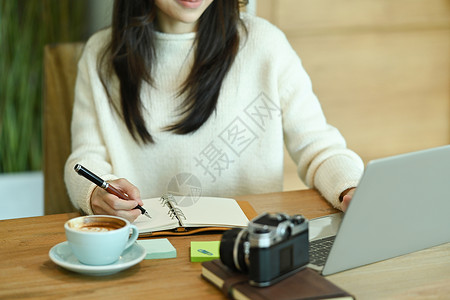穿白毛衣的年轻亚洲女人 拿着笔记着日记背景图片